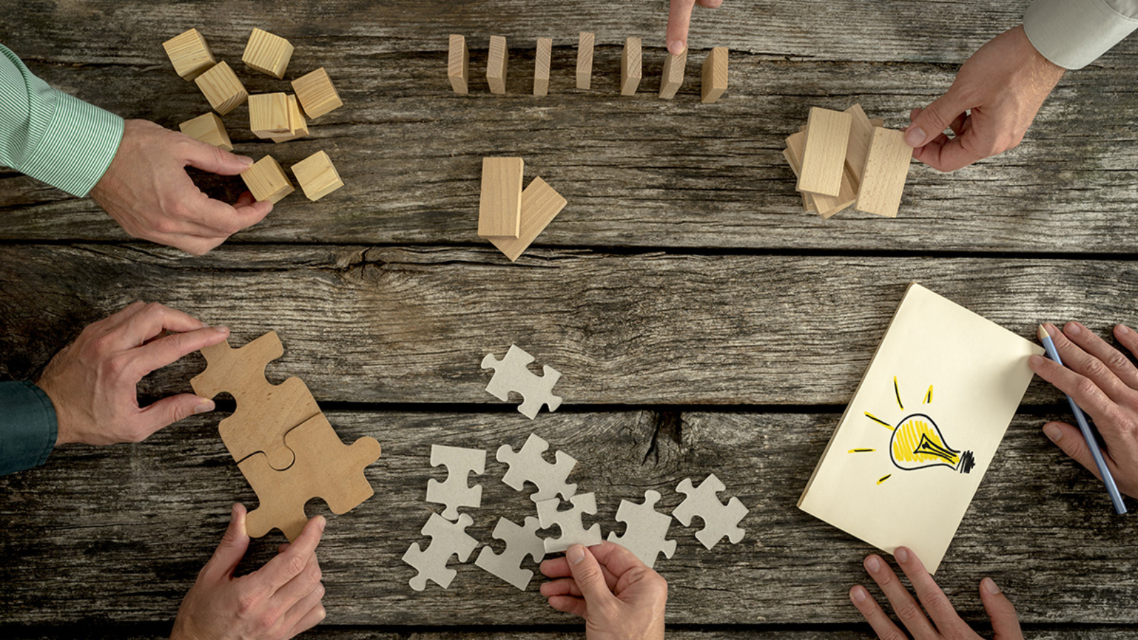 Businessmen planning business strategy while holding puzzle pieces, creating ideas with light bulb drawn on paper and rearranging wooden blocks. Conceptual of teamwork, strategy, vision or education.